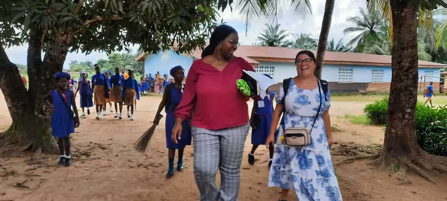 Natalie walking through a school compound with a Peace Corps Volunteer, schoolchildren behind them